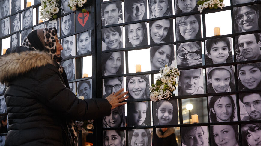 A woman touches victims' portraits as mourners attend an outdoor vigil for the victims of Ukrainian passenger jet flight PS752.